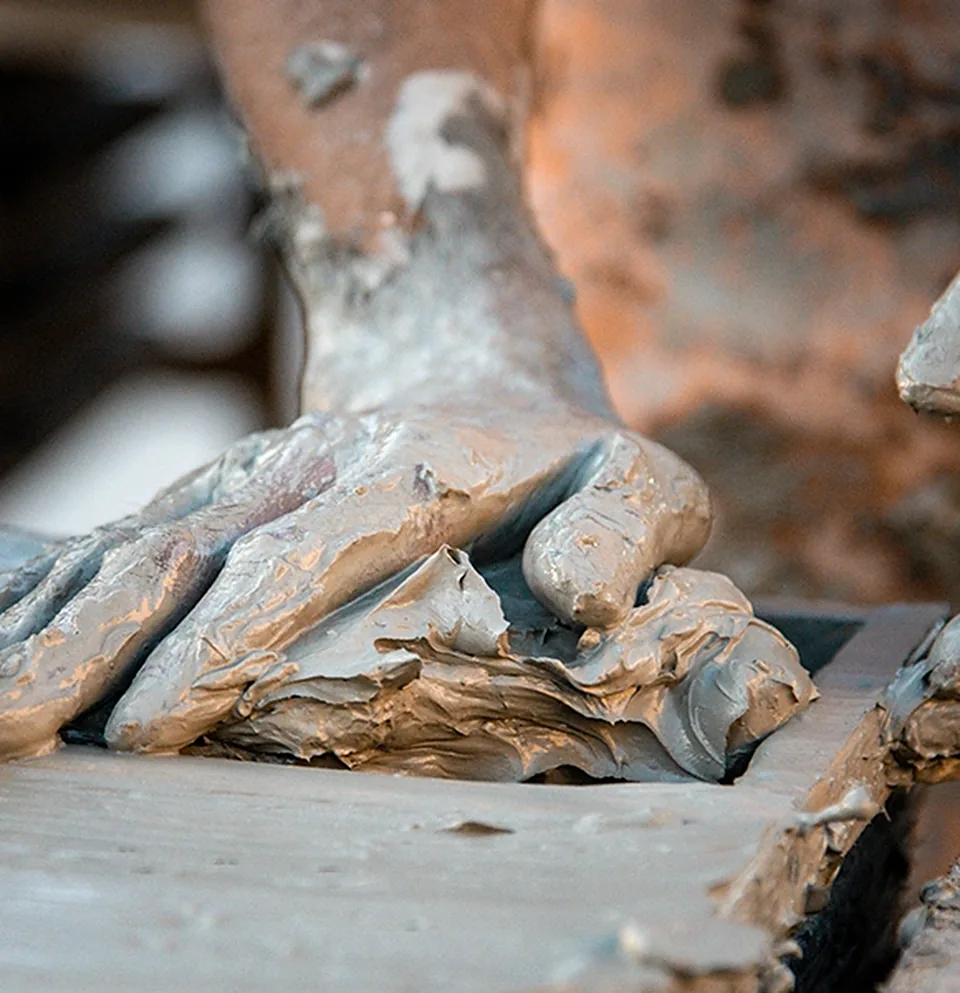 An artisan's hands pressing wet clay into a wooden tile mould, shaping it by hand before firing
