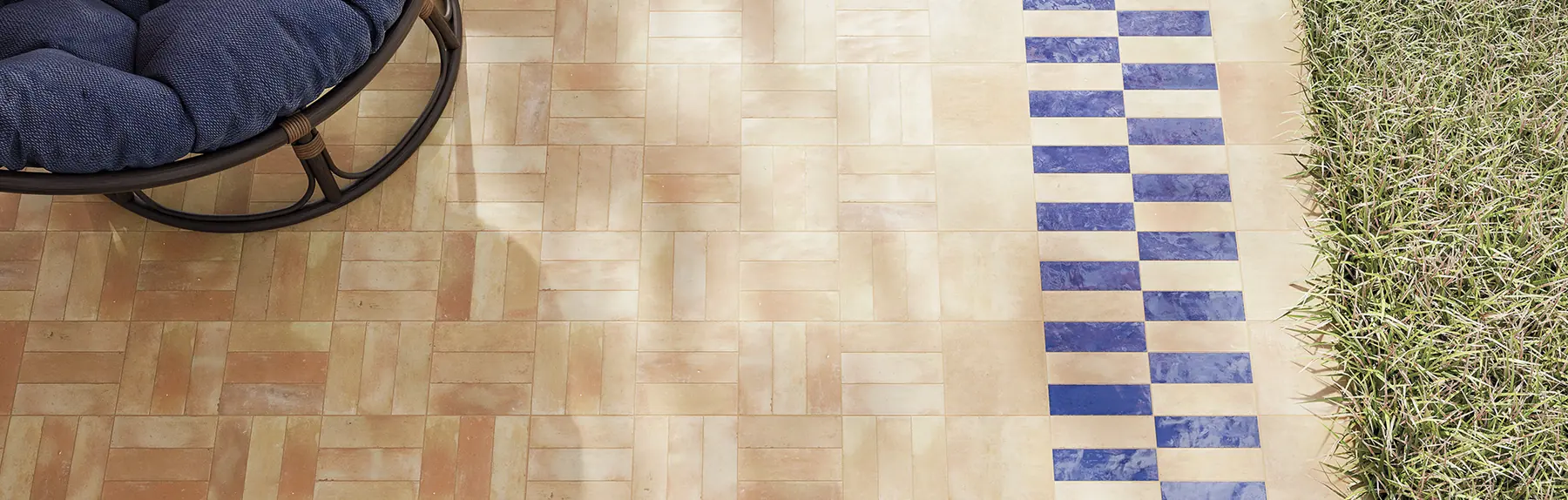 Terracotta bejmat terrace bordered with blue tiles where the paving meets the lawn