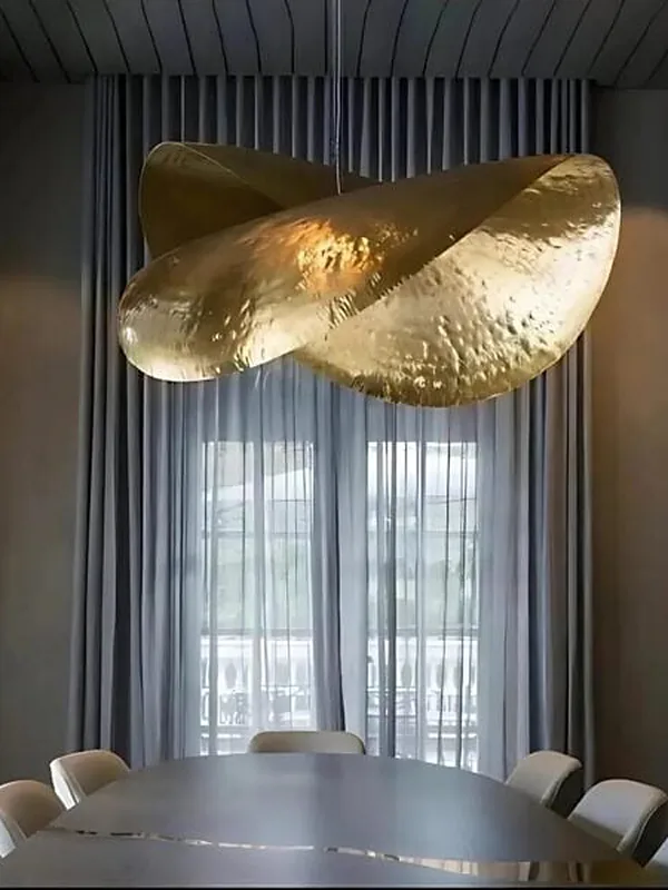 A sculptural hand-hammered brass pendant light above a dining table against sheer curtains