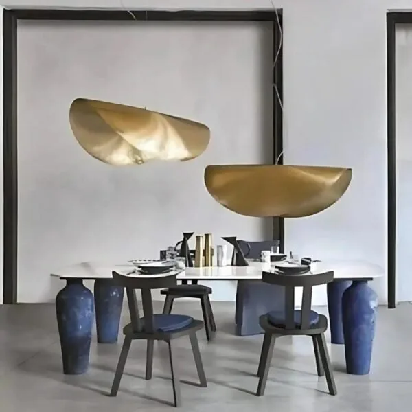 Two hammered brass leaf-shaped pendant lights at staggered heights above a dining table with blue glazed vessels