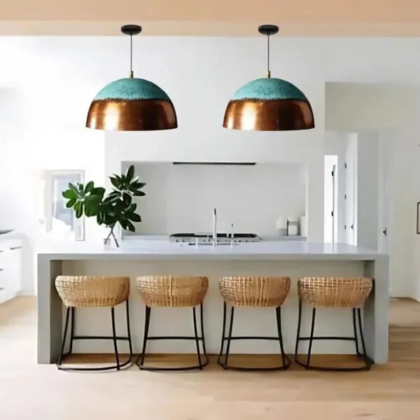 A pair of verdigris and copper dome pendant lights above a kitchen counter with woven bar stools