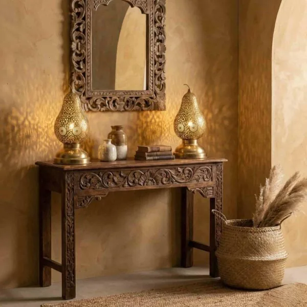 A pair of pierced brass pear-shaped table lamps on a carved wooden console table beneath an ornate mirror