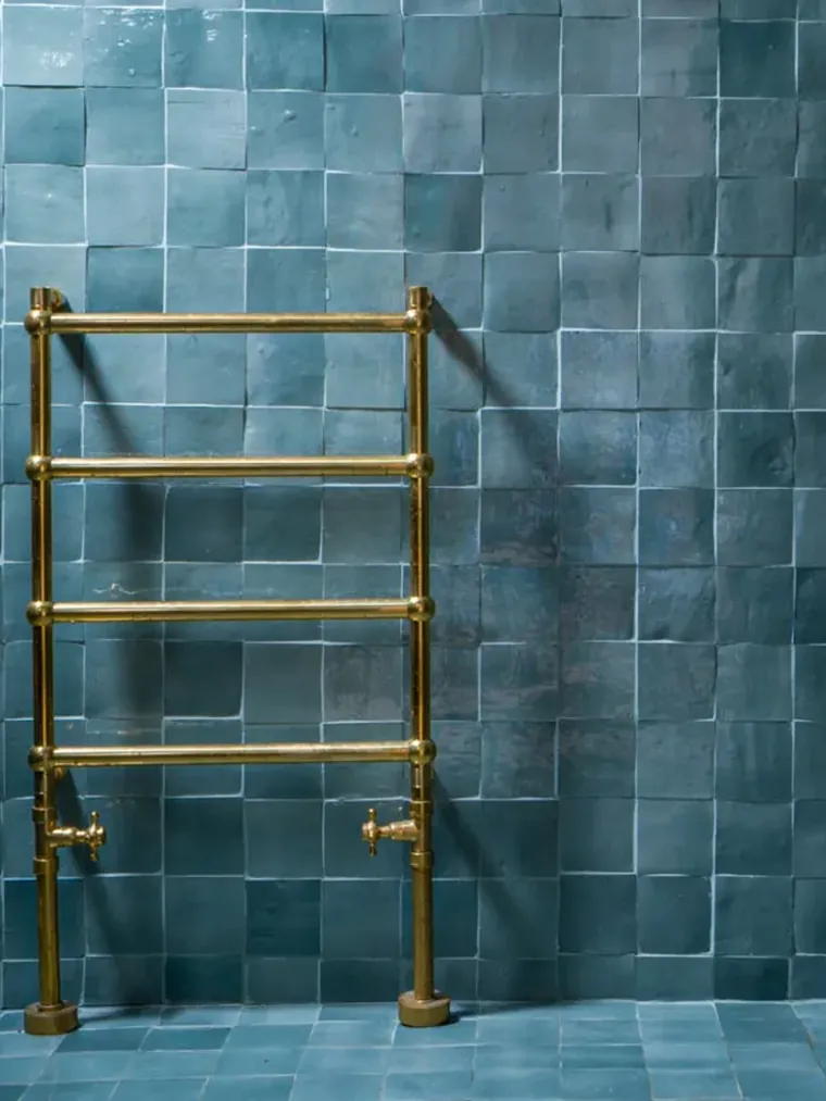 Deep teal glazed zellige tiles covering a bathroom wall behind a brass heated towel rail