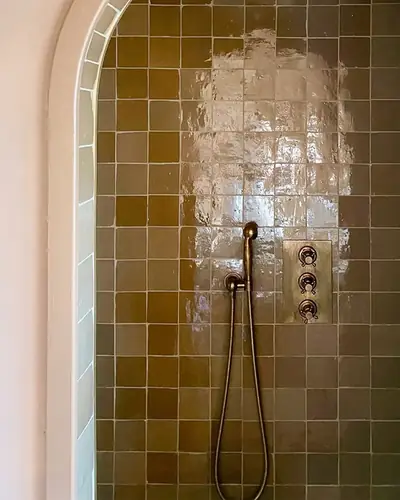 Bronze-brown glazed zellige lining an arched shower recess with a brass shower set