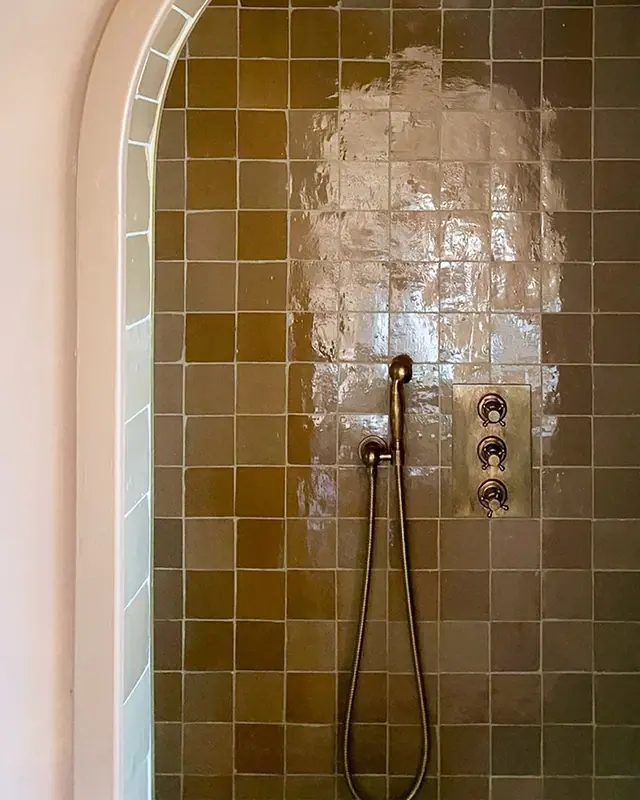 Bronze-brown glazed zellige lining an arched shower recess with a brass shower set