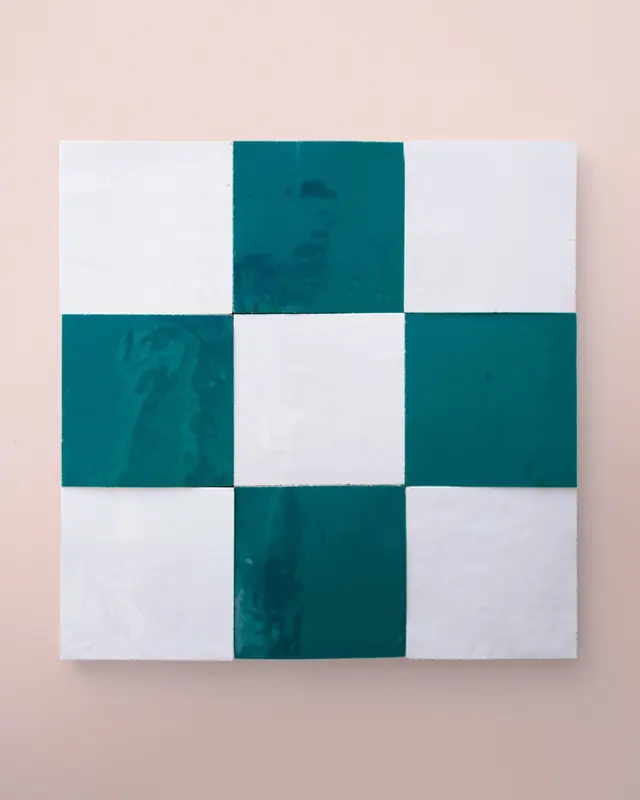 Teal and white zellige tiles set as a checked panel on a pale pink wall, the layout carrying the pattern rather than the grout