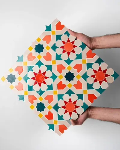 Hands holding a hand-cut zellige panel of red, teal and yellow stars on white