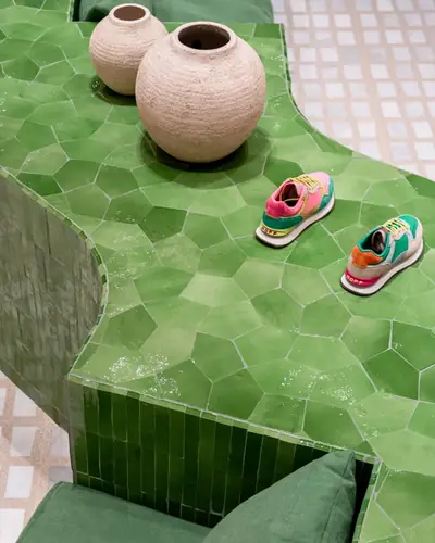 Bright green zellige cladding a seating platform and counter in a shoe shop