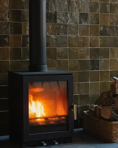 Dark olive zellige tiles forming the wall behind a black wood-burning stove