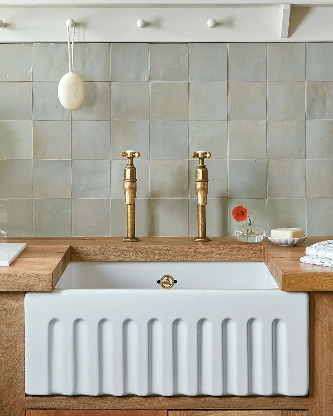 A pale green zellige wall above a white fireclay sink with brass taps