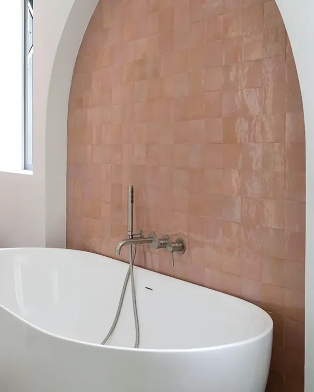 Terracotta pink zellige lining an arched recess above a freestanding bath