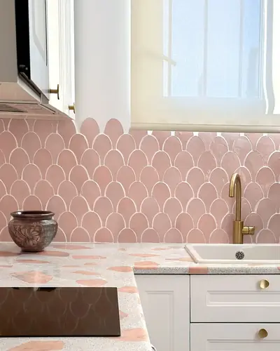 Pink scallop-shaped zellige tiles forming a kitchen backsplash behind a brass tap