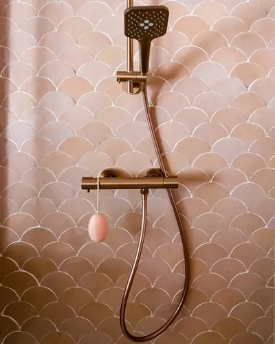 Pink scallop-shaped zellige covering a shower wall with a copper shower set
