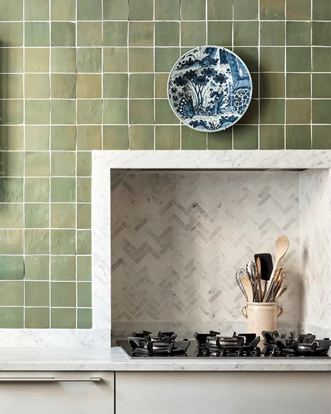 A pale sage green zellige wall framing a marble cooking niche, the tiles reading as a range of related tones