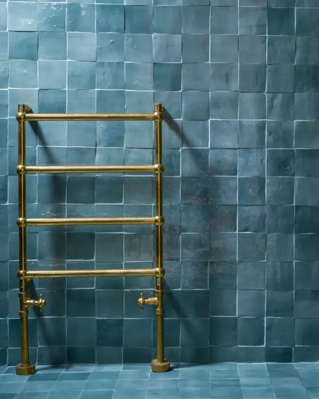 A deep teal zellige bathroom wall behind a brass heated towel rail