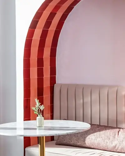 Pink plastered terrace arch banded with red zellige tiles above a seating booth