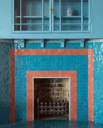 Turquoise zellige wall with an orange-framed fireplace surround in a blue kitchen