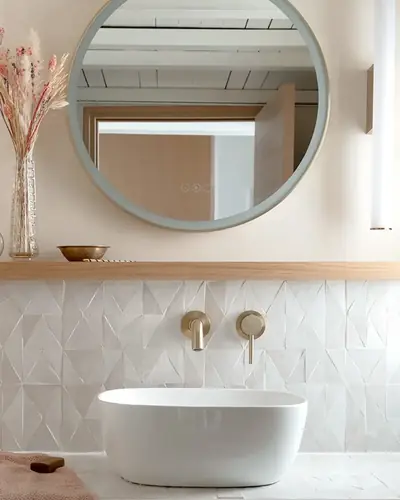 White zellige backsplash with a shaped upper edge behind a bath and round mirror